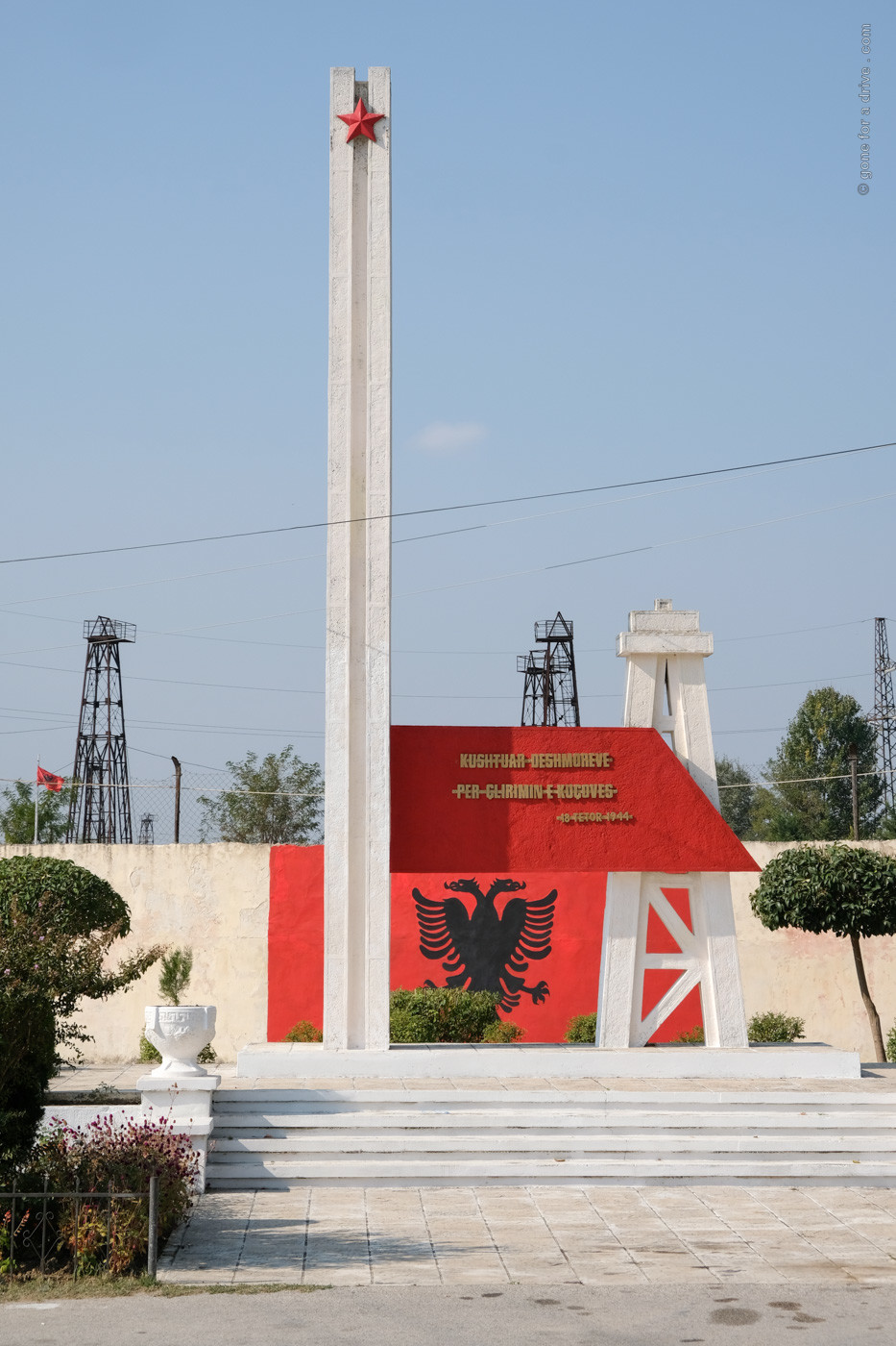 Denkmal und dahinter liengende Ölfördertürme in Kucova, Albanien.